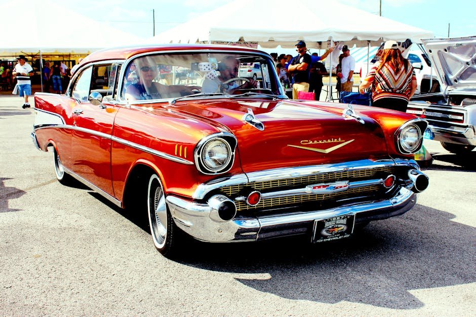 A vintage red 1957 Chevrolet showcased at an outdoor car exhibition with attendees.